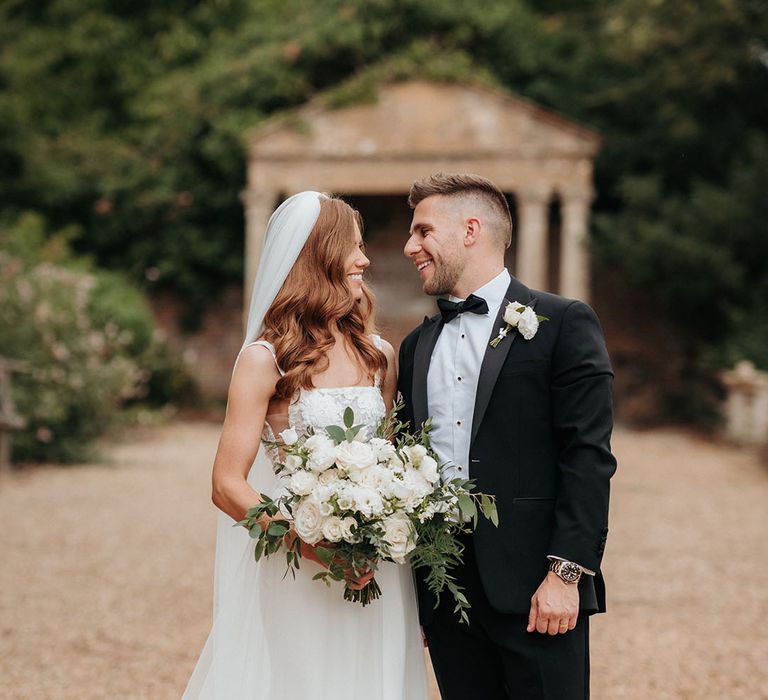 Groom in black tuxedo with the bride in a classic white wedding dress holding a white wedding bouquet 