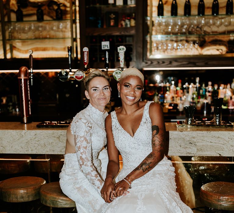 Two brides sitting next to each other at the wedding bar with flash photo 