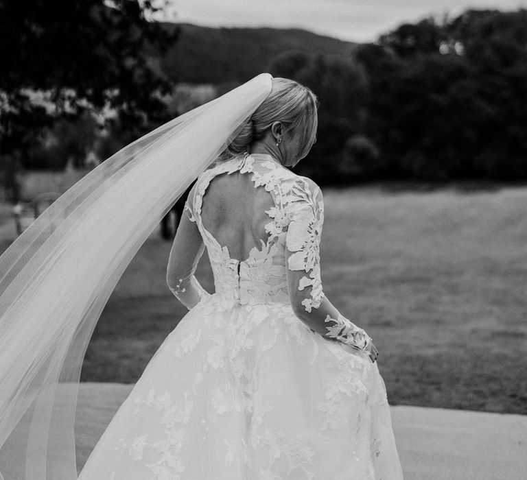 Bride with cutout back detail on lace long sleeve wedding dress with cathedral length veil 