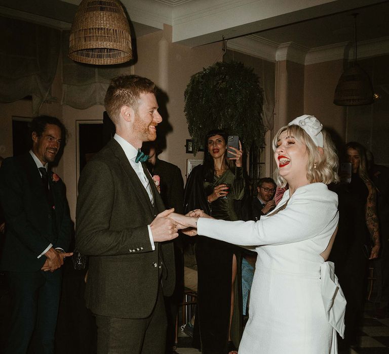 Bride in long sleeve square neck short wedding dress with white Doc Marten shoes and headband with groom in black suit 