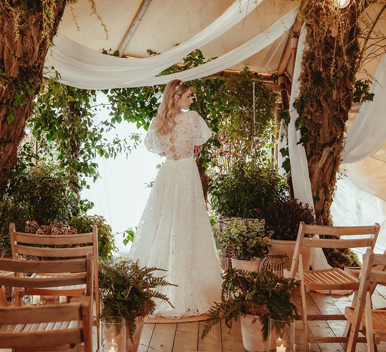 Bride in short sleeve floral lace wedding dress from Love And Loved Bridal with foliage and white drapery decorations 