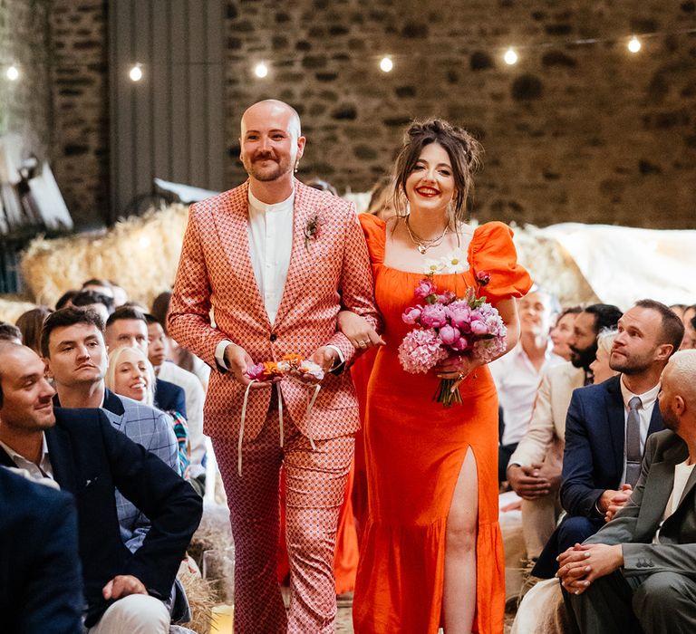 Bridesman and bridesmaid walk down the aisle together in orange outfits 