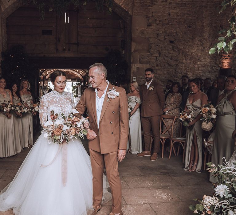 Father of the bride in a brown wedding suit walks bride down the aisle at rustic Stone Barn wedding