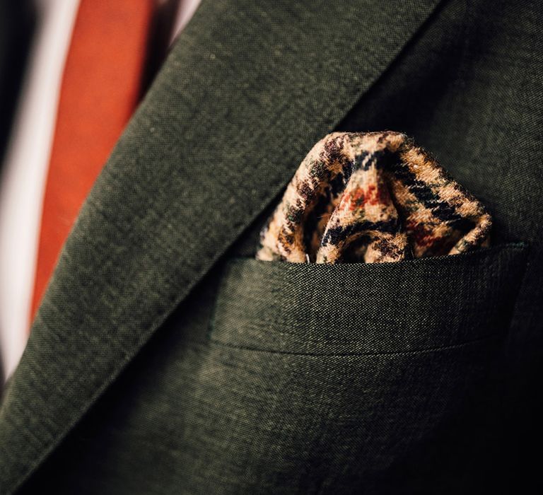 Groom with dark green wedding suit wearing an orange tie and houndstooth pocket square 