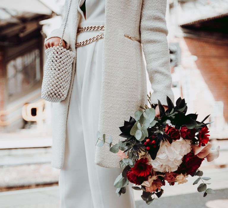 Bride in Massimo Dutti jumpsuit with red shoes and red, white and foliage bouquet 