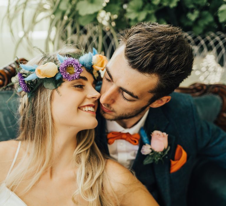 Bride wears rose and pampas grass and other assorted flowers crown and embraces with groom with orange details