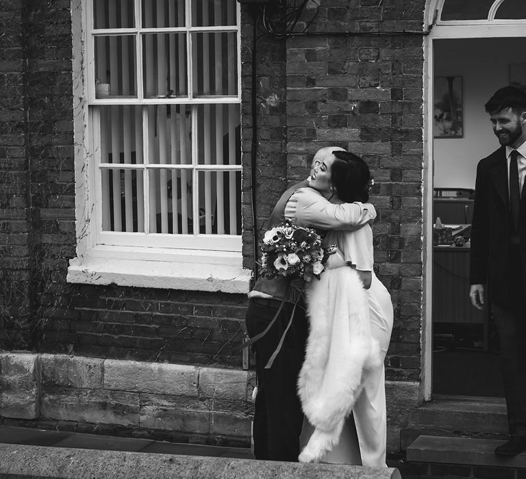 Bride with red carnation bouquet hugging guest at wedding