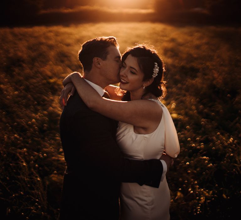 Bride & groom embrace during golden hour with sun setting