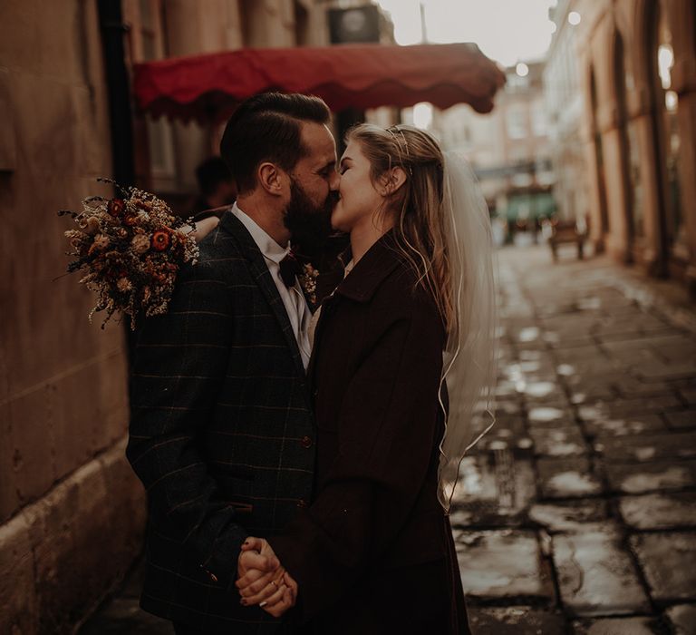 Bride clutches dried flower bouquet as she kisses new husband at city elopement