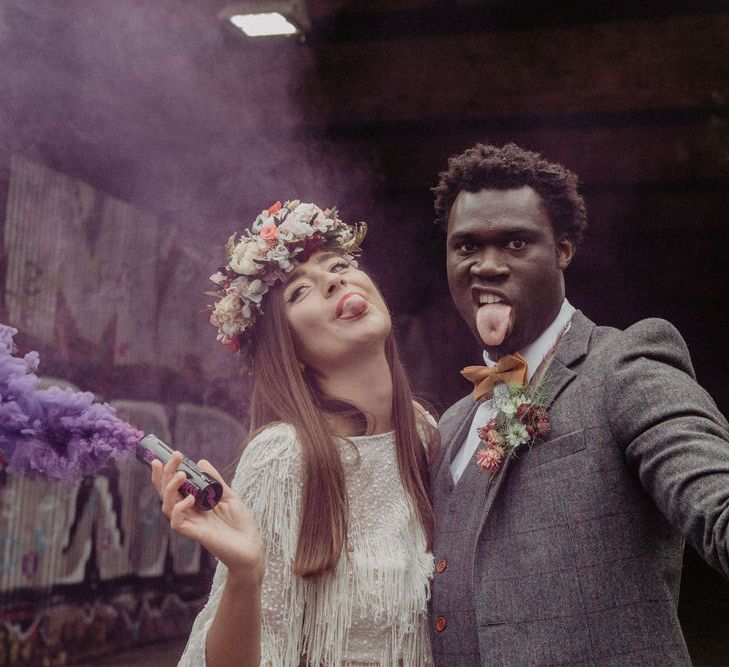 Wedding couple stick out their tongues at the camera, bride holds a purple smoke bomb