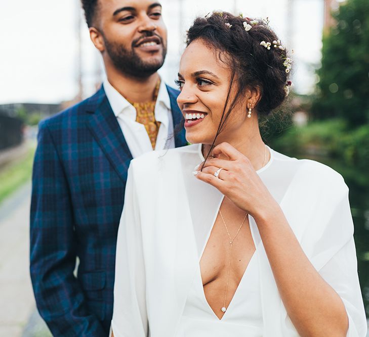 A bride stands in front of a groom and stop her hair blowing in to her face