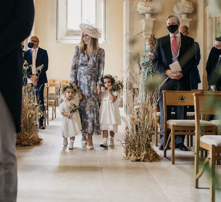 Flower girls in white dresses and flower crowns walking down the aisle with dried flower decor 