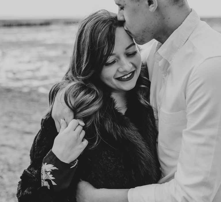 Intimate black and white portrait of the groom-to-be kissing his Fiancee's head 