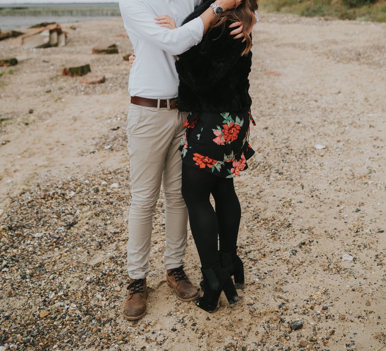 Groom-to-be in a white shirt and stone chinos brushing the hair off his bride-to-be's face during their beach engagement session 