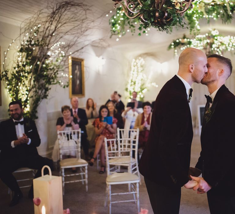 Gay couple kissing at the altar in burgundy tuxedo jackets 