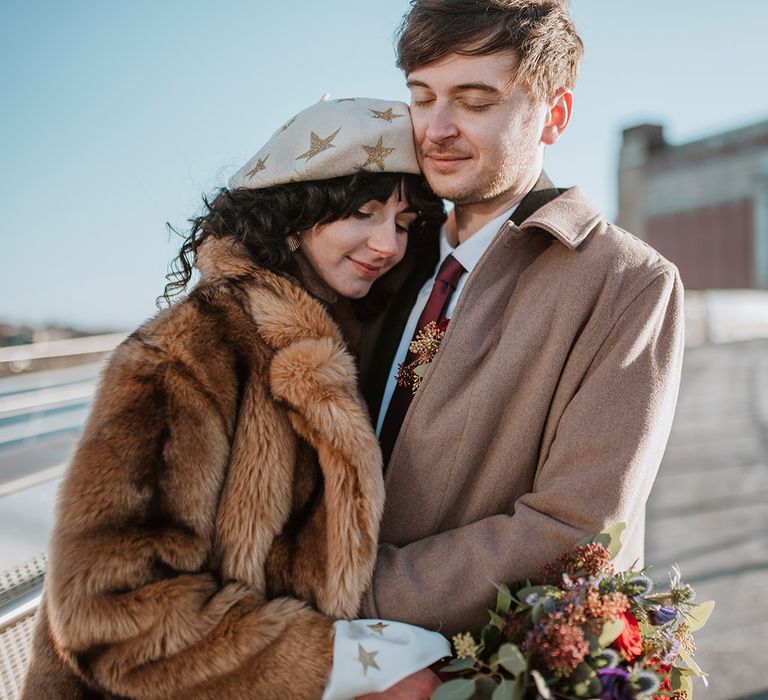 Bride cuddles groom in coat and beret hat