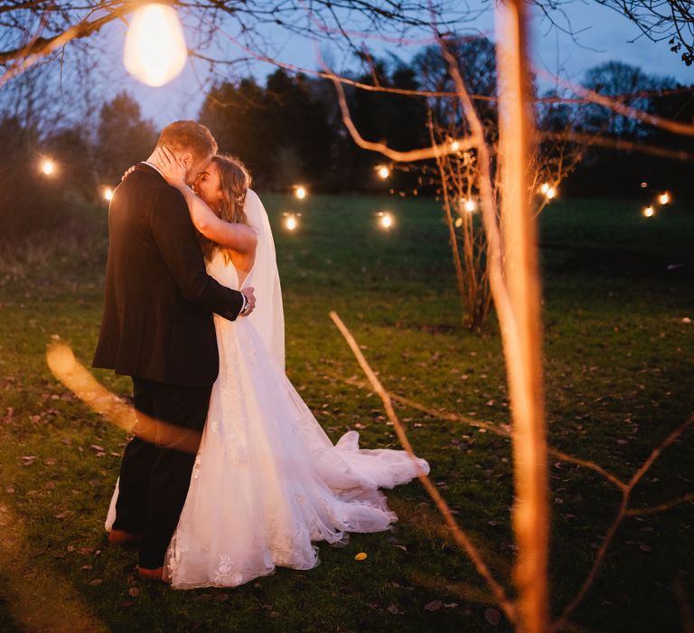 Bride & groom embrace surrounded by lights outside