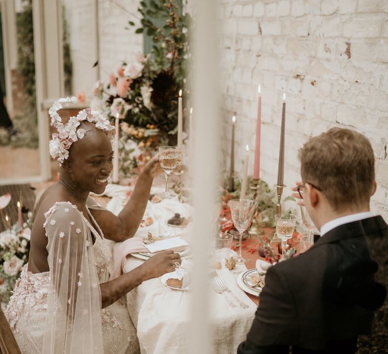 Bride with alopecia sitting at her intimate elopement reception in an embellished blush pink wedding dress with watteau train and floral headdress 