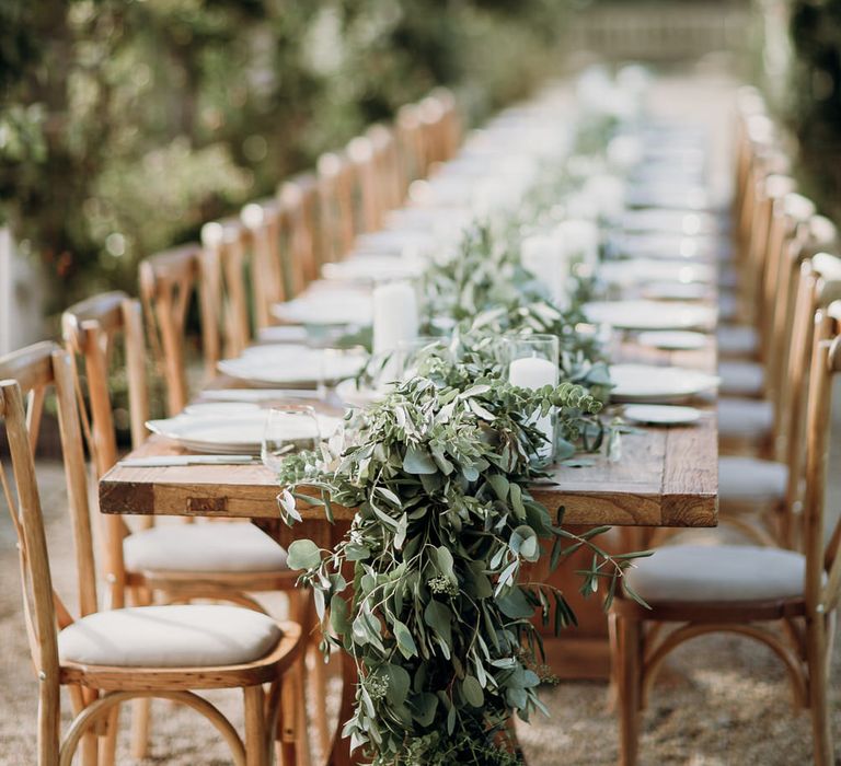 Rustic wooden wedding table with light wooden chairs and wedding table garland under canopy of foliage at Euridge Manor wedding