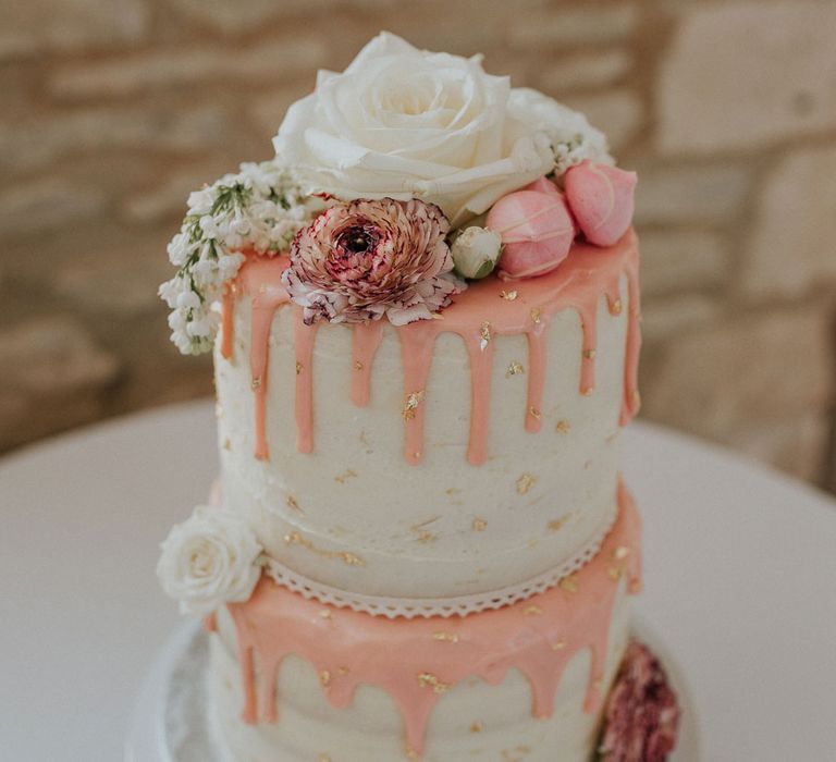 White two tier wedding cake with pink dripping icing, gold leaf details and white rose decor