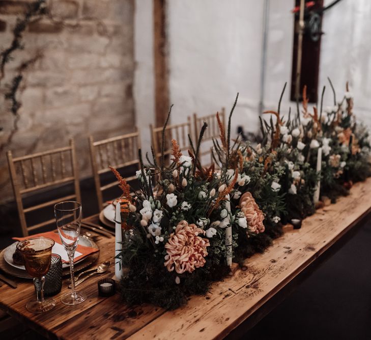 Orange and white flowers mixed with foliage and candles for wedding reception decor 