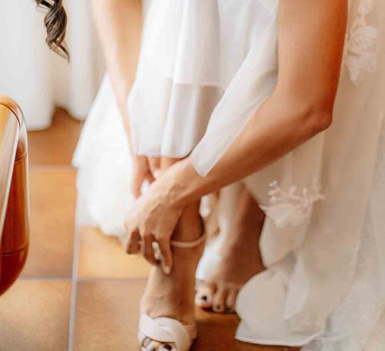 Bride fastens her white wedding shoes for Italian wedding