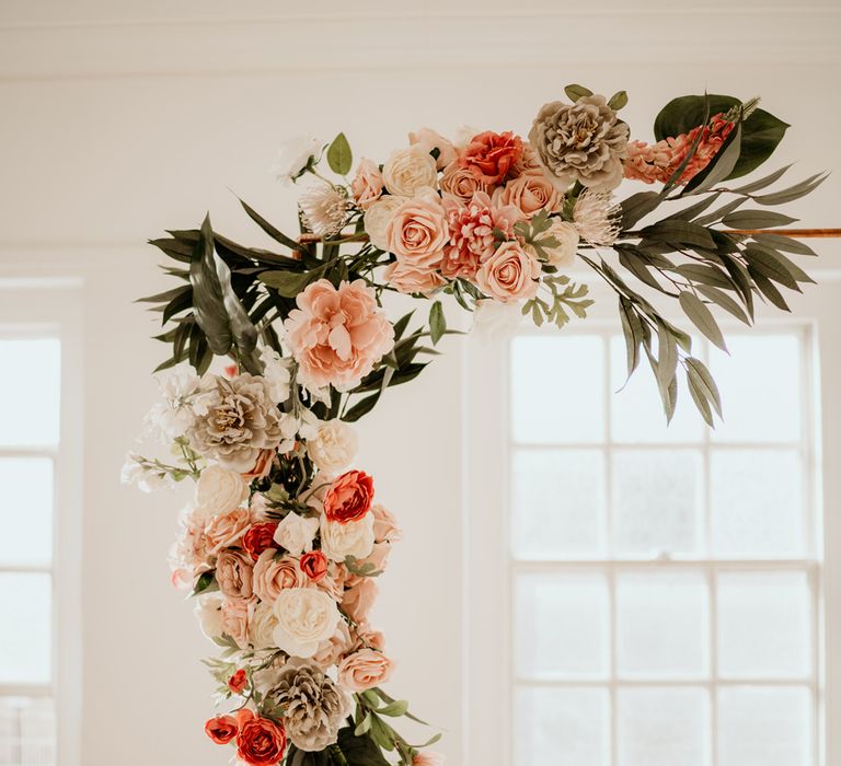 Dahlias, roses and ranunculus peach and coral wedding flowers decorating the copper frame altar