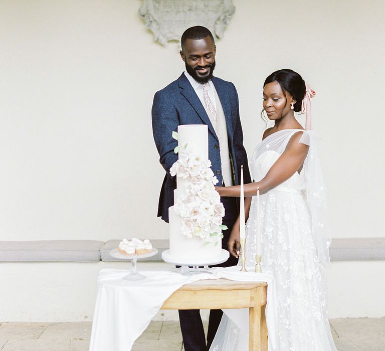 Bride and groom cutting into their four tier white wedding cake with cascading flower decoration by Mon Annie Cakes