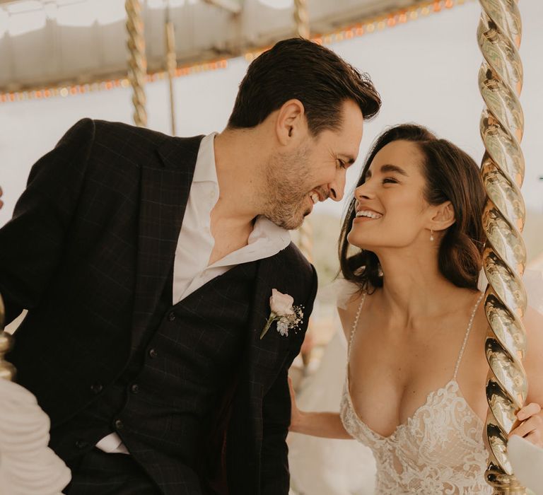 Groom in a three-piece check suit looking at his bride in a lace wedding dress with thin straps 