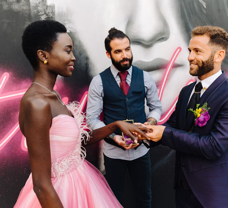 Bride & groom during wedding ceremony in front of graffiti mural and celebrant