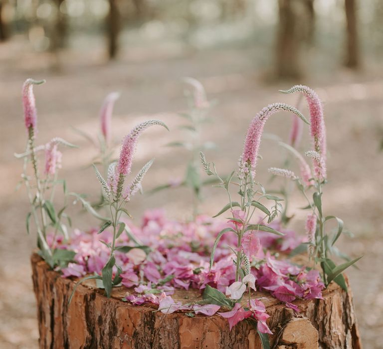 Tree stump decorated with pink flowers and petals at enchanted forest wedding in Italy 