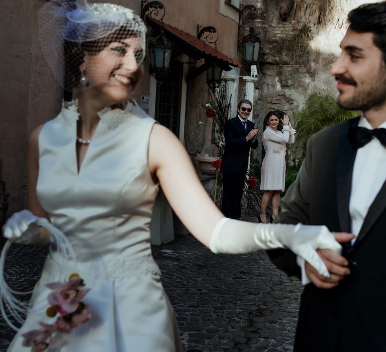 The bride and groom leaving their wedding ceremony wearing a vintage style wedding dress and tuxedo