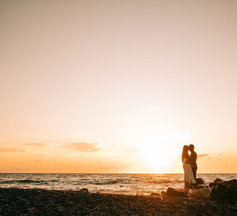 Bride & groom stand on rocks as they watch the sun set 