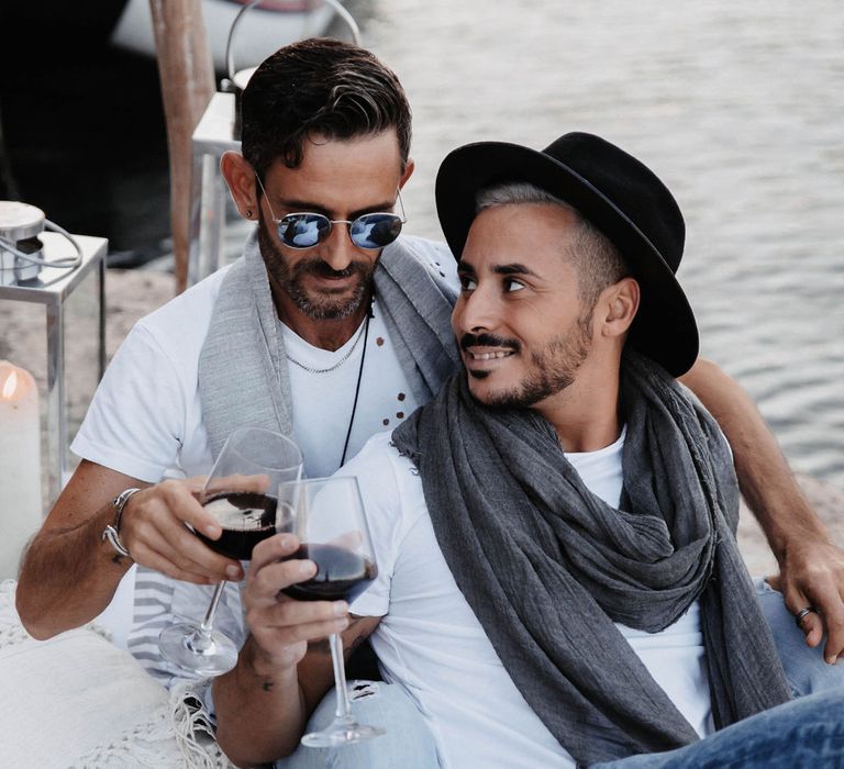 Grooms laugh together and drink red wine during their engagement session