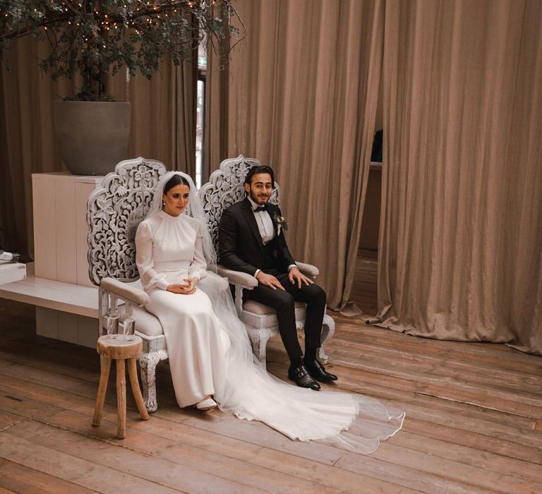 Bride & groom sit together on silver thrones