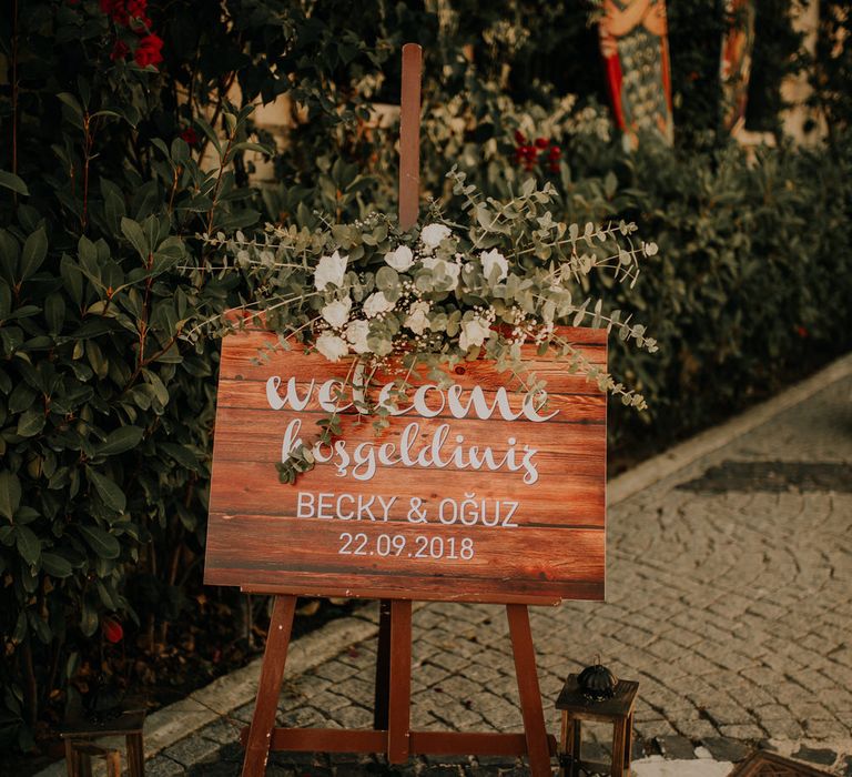 Wooden wedding welcome sign with white calligraphy script and white flower garland decoration