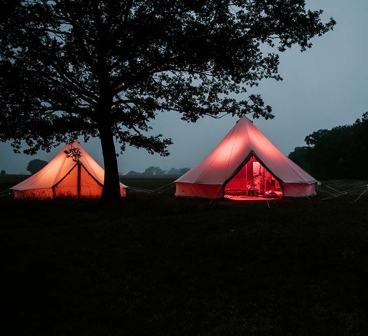 Three teepees lit up with orange, pink and blue lights outside at festival themed wedding