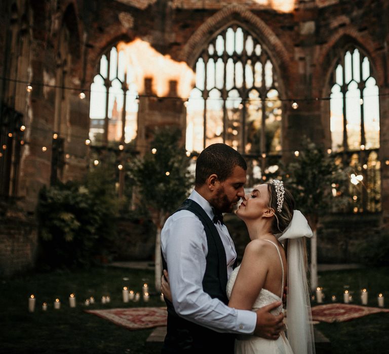 Stylish bride and groom kissing in an open air church with festoon light decor 