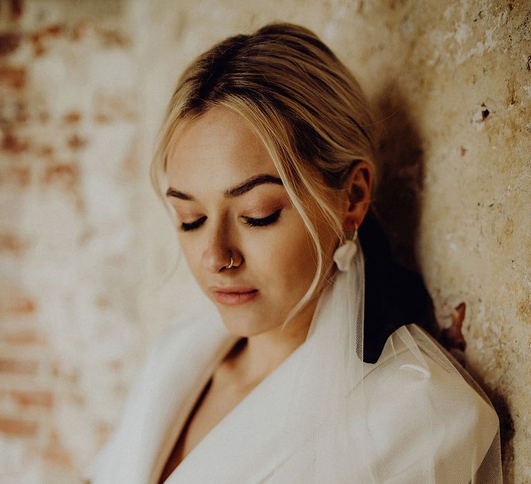 Bride in a white blazer with sheer veil and shimmering eye shadow crossing her arms showing her beige nail art 