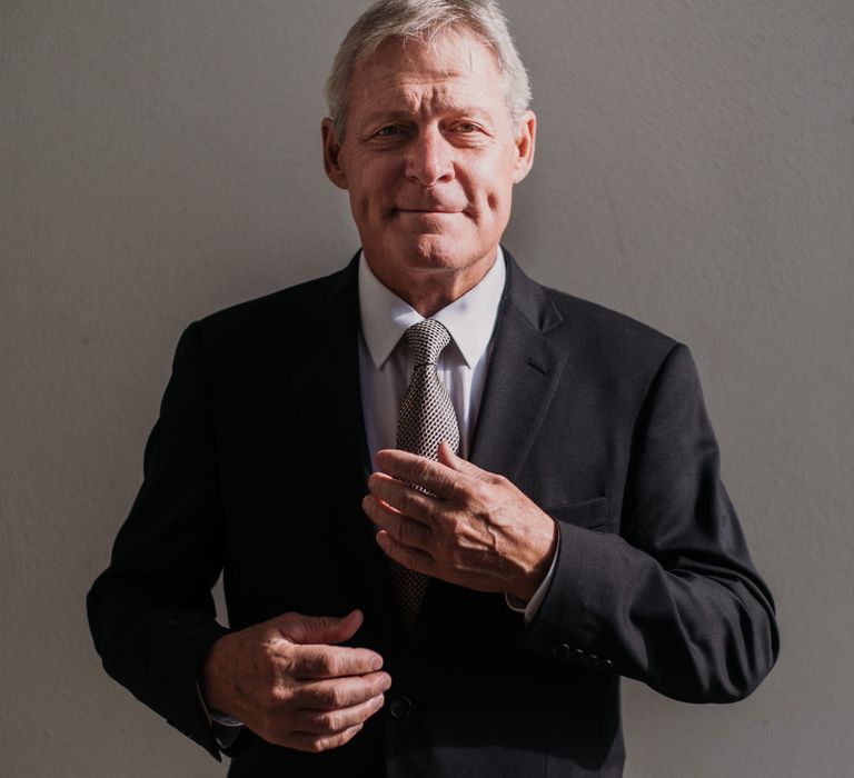 Groom looks to the camera whilst doing up silver patterned tie and wearing black jacket