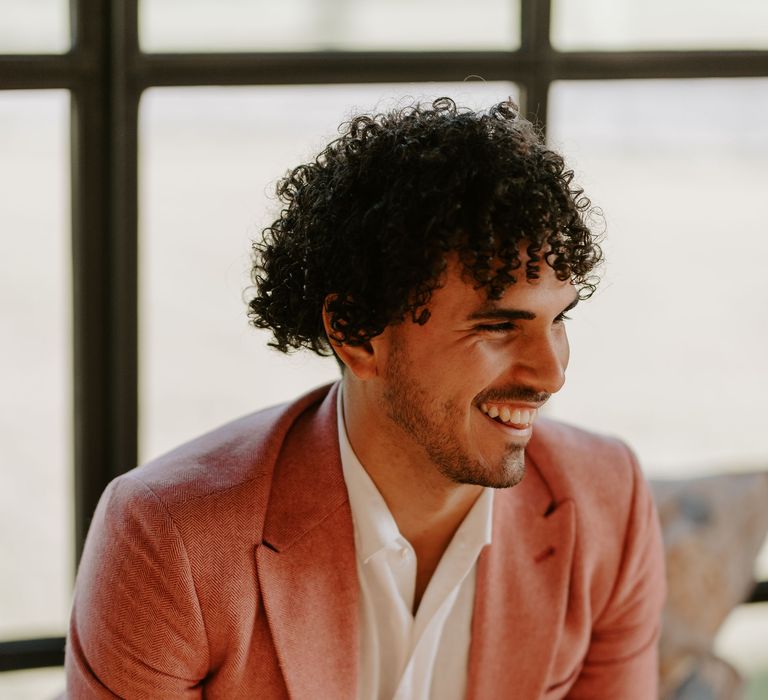 Stylish groom with naturally curly hair in an open white shirt and red blazer 