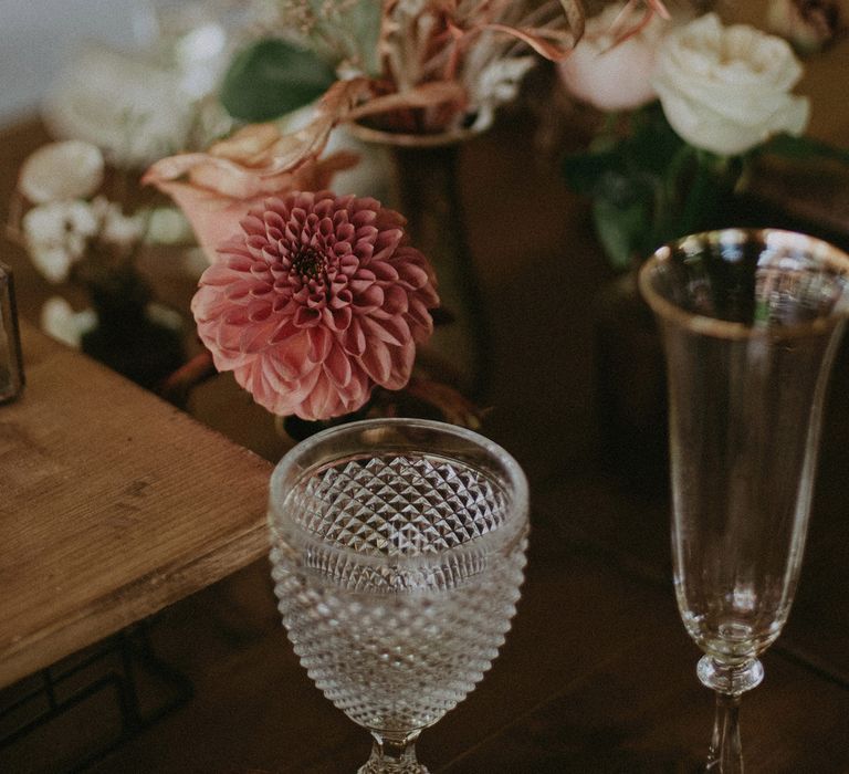 White, brown and pink dried flowers on wooden table with clear diamond cut wine glass and gold rimmed tulip champagne flute at wedding reception with burnt orange wedding theme