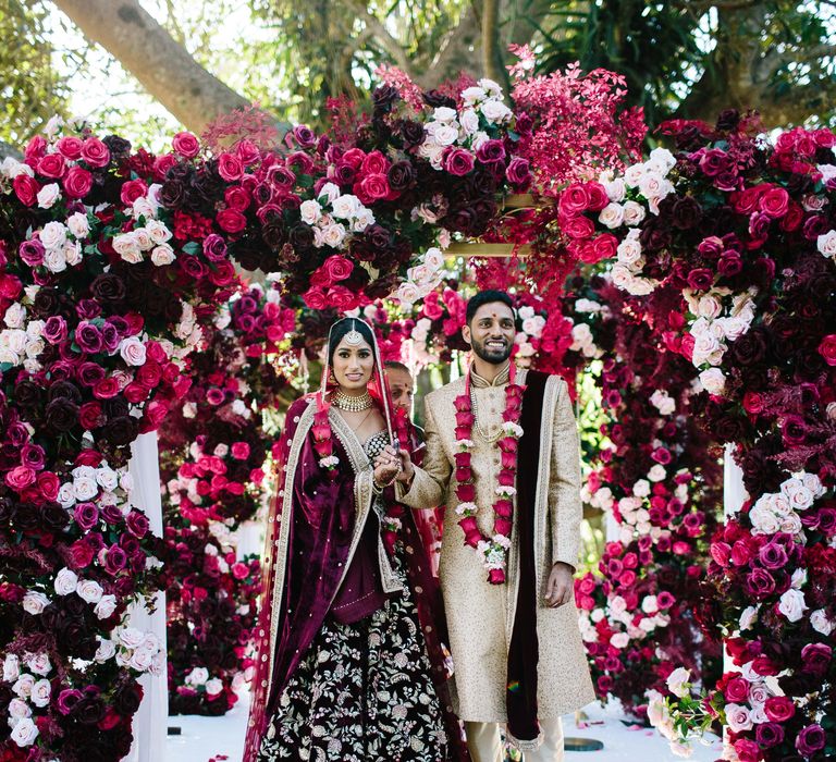 Bride & groom stand in front of incredible bright and vibrant florals on their wedding day