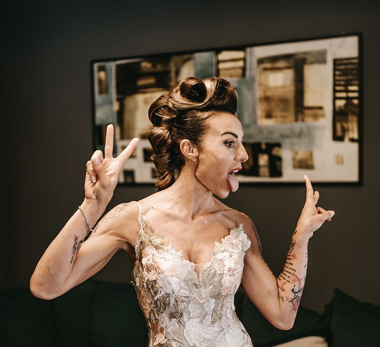 Bride sticks out her tongue and does peace sign with hands as she wears her bridal gown and hair in modern and stylish hairstyle