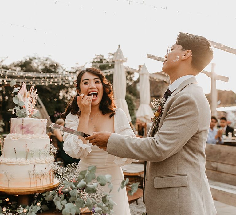 Bride & groom laugh as they cut their wedding cake outdoors