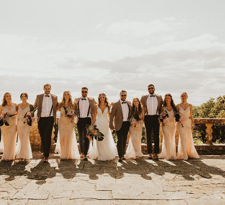 Bride & groom stand with their wedding party outdoors as the sun begins to set