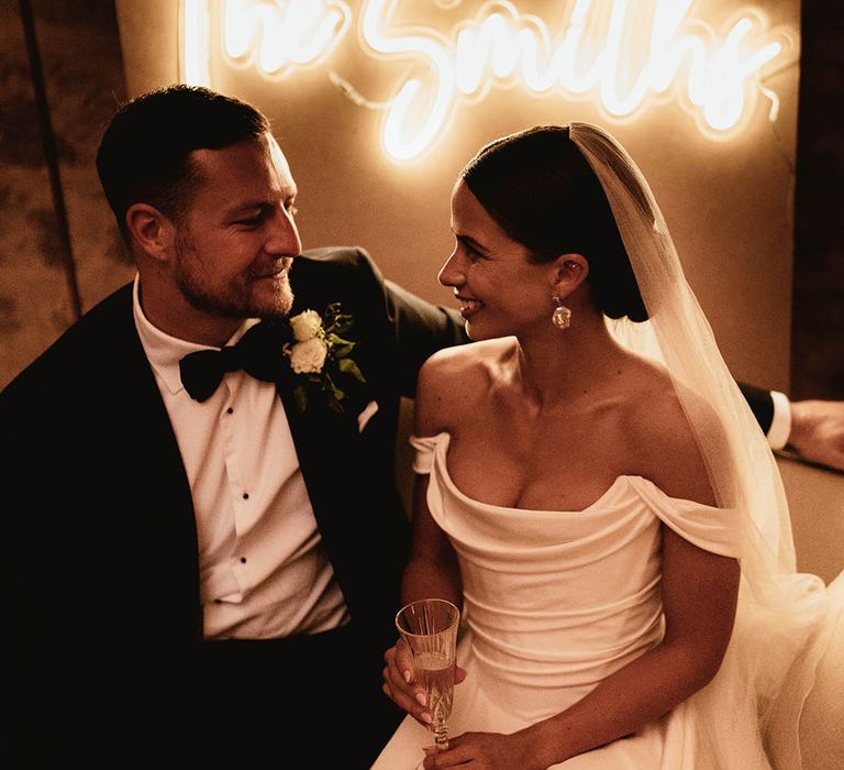 Bride & groom sit in front of personalised neon sign on their wedding day