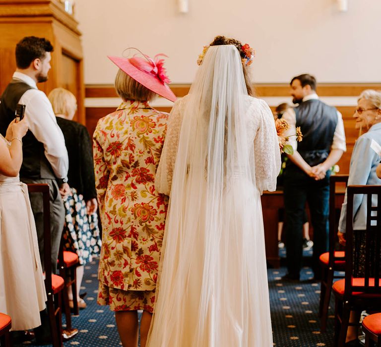 Bride walks down the aisle with her mother on her wedding day wearing homemade wedding gown and veil