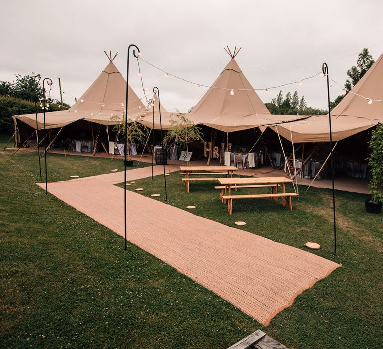 Large garden wedding tipi with wooden benches and shepherds hook lights for rustic wedding reception