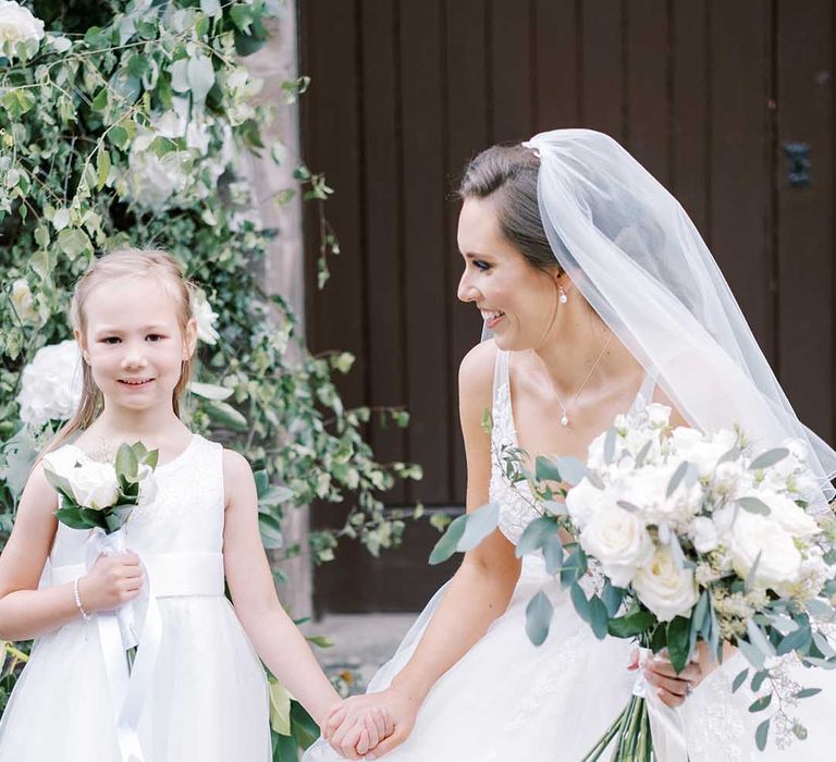 Classic bride in a tulle wedding dress and veil holding hands with the flower girl in a white dress